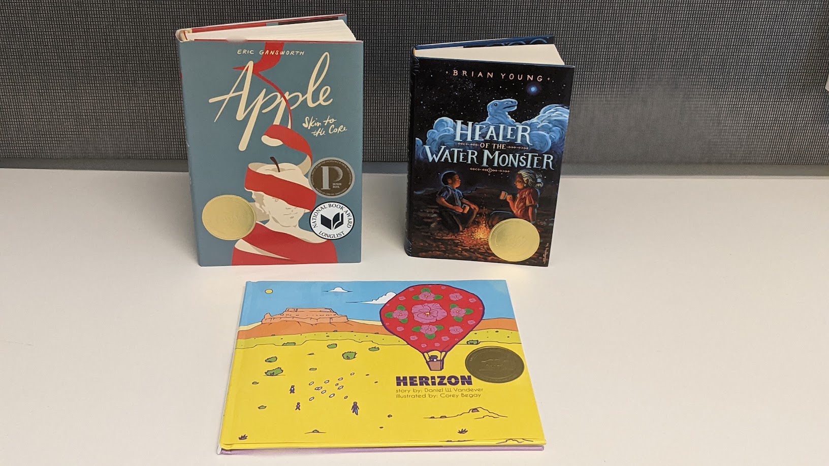 Three books: Apple skin to the Core, Healer of the Water Monster, and Herizon on a table